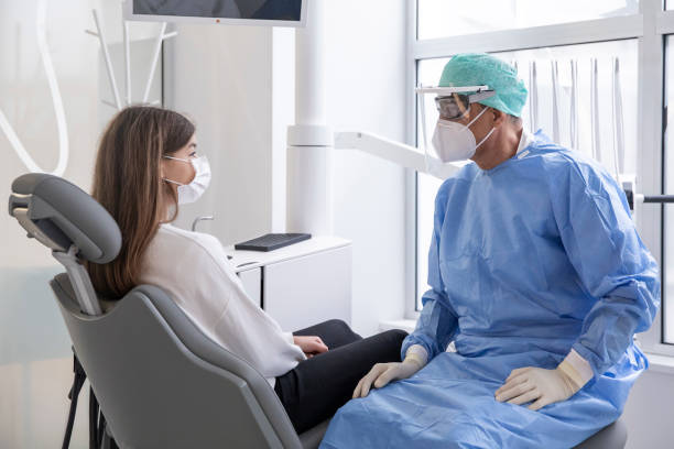 Dentist talks to patient in dental examining room stock photo