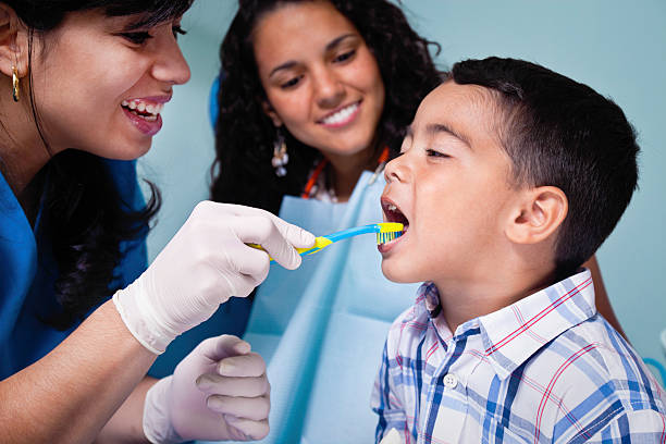 Dentist teaching toothbrush use to child patient stock photo