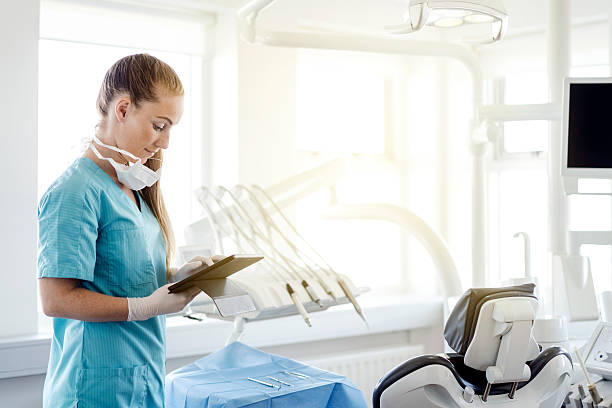 dentist using digital tablet by chair in clinic - tandarts stockfoto's en -beelden
