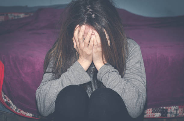Depressed and lonely girl abused as young sitting alone in her room feeling miserable and anxiety cry over her life, dark image stock photo