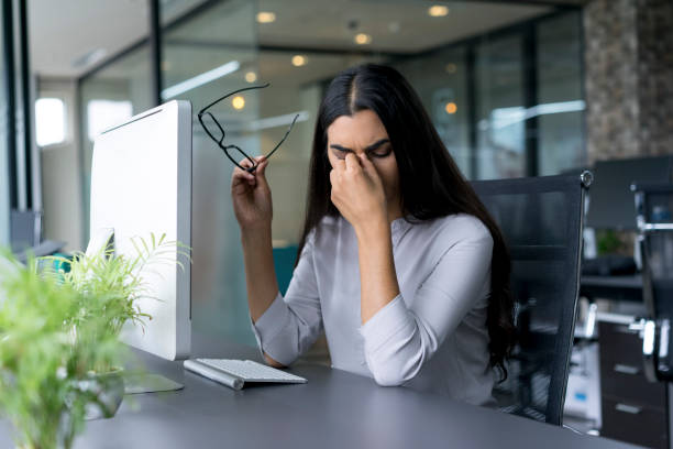 Depressed businesswoman rubbing eyes in office stock photo