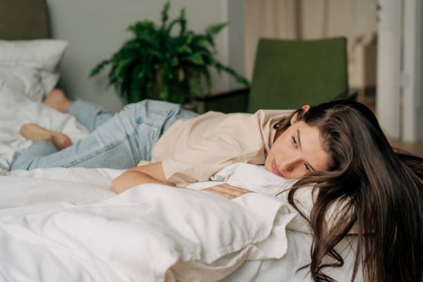 Depressed sad young woman lying on bed stock photo
