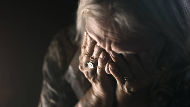 Depressed Senior Woman Alone In The Dark - Sadness, Mental Health, Negativity Desperate senior crying in a dark room. Perfectly usable for a wide range of topics like depression, loneliness or mental health in general. grief stock pictures, royalty-free photos & images