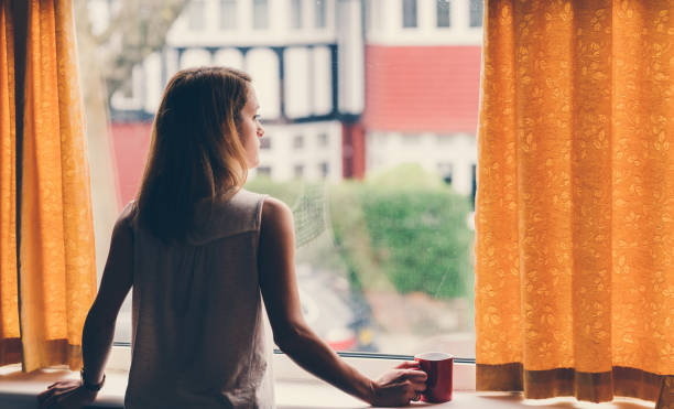 Depressed woman at home Thoughtful woman at home looking through the window staring stock pictures, royalty-free photos & images