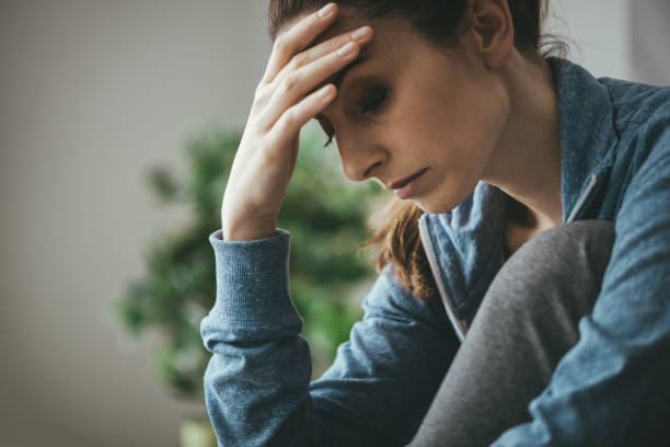 Depressed woman at home Sad depressed woman at home sitting on the couch, looking down and touching her forehead, loneliness and pain concept Emotional Pain stock pictures, royalty-free photos & images