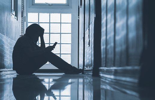 Depressed woman sitting alone and looking smartphone with holding her head on corridor in front of room at apartment in low key style