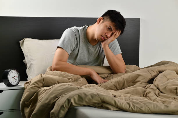 Depressed young Asian man sitting in bed cannot sleep from insomnia stock photo