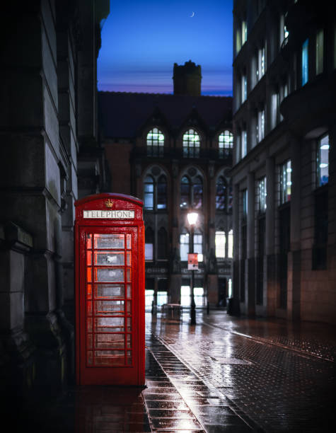 Deserted street at night with traditional royal red British telephone box lit up light reflecting on water after rain clear night sky moon eerie view in Birmingham city centre England UK A cold night in the city centre with no one around due to the pandemic lockdown, this would normally be a very busy thoroughfare. red telephone box stock pictures, royalty-free photos & images