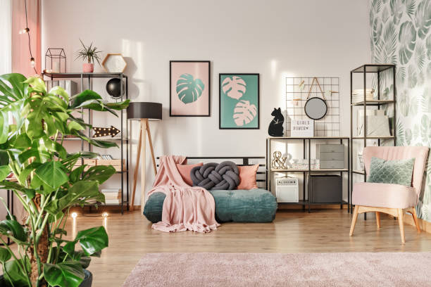 Designer sofa in living room Knot pillow on a designer emerald green mattress sofa in a living room interior with industrial furniture and a retro powder pink chair and plants femininity stock pictures, royalty-free photos & images