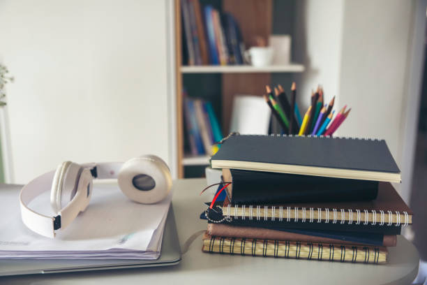 Desk for student education concept. Book, and pencil for study for exam. Laptop and headphone placed on white School table with bookshelf background for student plan to work at home. stock photo