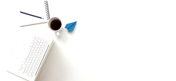 Directly above view of a laptop, notepad, blue paper plane and cup of coffee on pure white background.