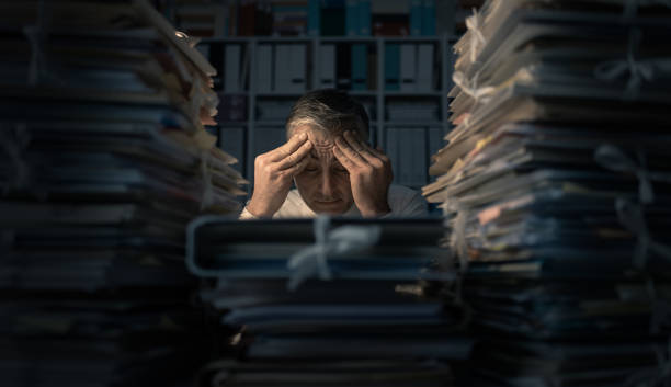 Desperate businessman working late Desperate businessman working in the office late at night and overloaded with work, his desktop is covered with paperwork: business management and deadlines concept overworked stock pictures, royalty-free photos & images