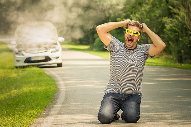 Desperate guy kneeing on the road because of broken car stock photo