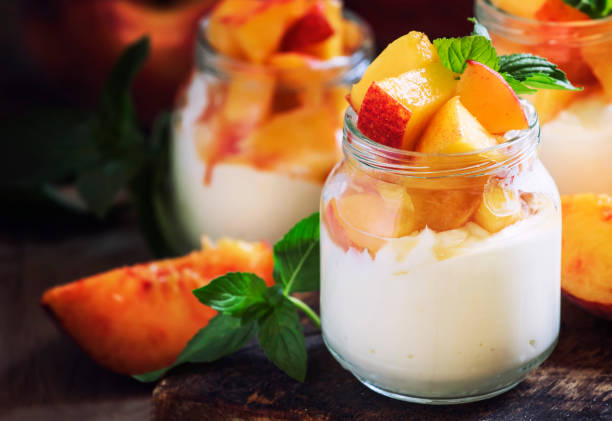 Dessert with sweet peaches, cottage cheese and whipped cream, served in glass jars, vintage wooden background, selective focus Dessert with sweet peaches, cottage cheese and whipped cream, served in glass jars, vintage wooden background, selective focus peach smoothie stock pictures, royalty-free photos & images