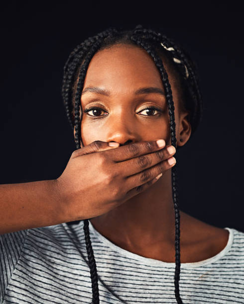 Destroy what stifles you Studio shot of an attractive young woman covering her mouth with her hand against a black background me too social movement stock pictures, royalty-free photos & images