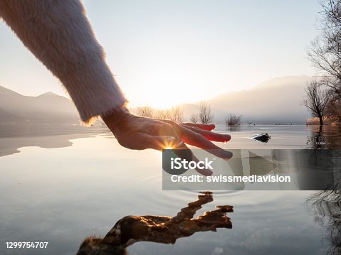 istock Detail of hand touching water surface of lake at sunset 1299754707