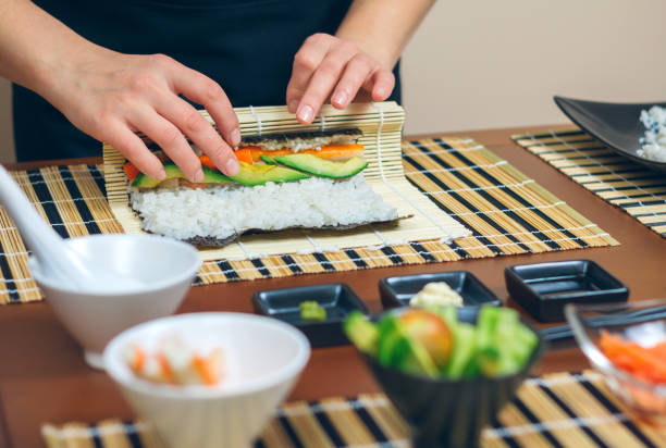 Detail of hands of woman chef rolling up japanese sushi stock photo