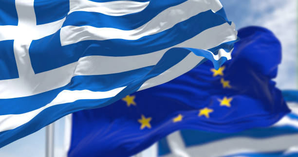 Detail of the national flag of Greece waving in the wind with blurred european union flag in the background on a clear day stock photo