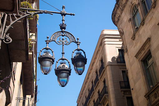 Detail of typical street lamp with facade of old buildings near Sant James (Sant Jaume) Square in Barcelona, Spain, place where City Council of Barcelona and Autonomous Goverment of Catalonia are located.