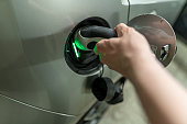 istock Detail view at a mans hand with is plugin the electric charging wire and plug into his e-automobiles fuel cap. Green light for the active charhing process. 1340173245