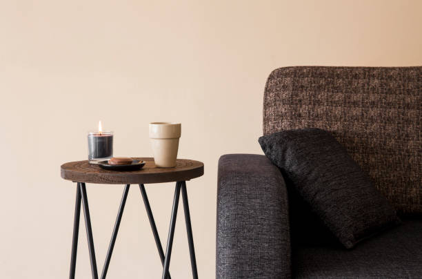 Vista detallada de la moderna mesa baja redonda de metal de madera con taza de capuchino, velas de vidrio ardiendo al lado del sofá. Vista detallada de la moderna mesa baja redonda de metal de madera con taza de capuchino, velas de vidrio ardiendo al lado del sofá. mesa de cafe fotos e imágenes de stock