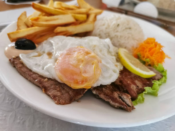 Detailed view of a tipical portuguese fast fried meal called bitoque, suite fried potatoes, rice, fried eggs and grilled beef steak stock photo