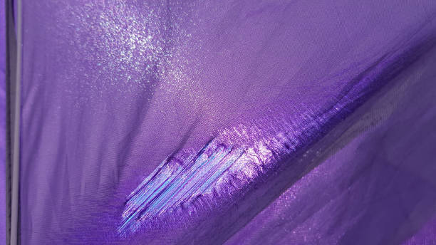 Details of old beach sunshade. Purple lacerated fabric surface with worn textile structure closeup. Sun is shining through torn textile tent with threads inside hole in fabric. stock photo