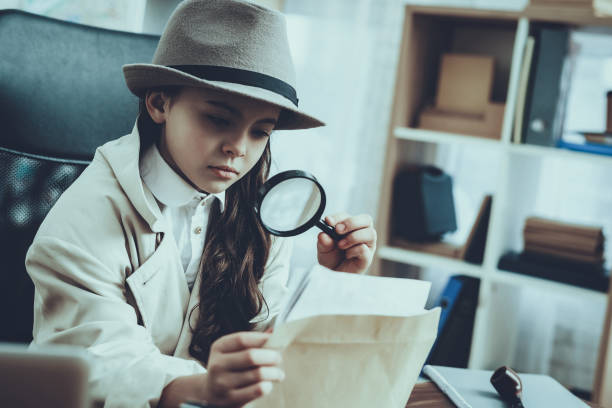 Detective is Working in Private Detective Agency Detective is Working in Private Detective Agency. Detective is Caucasian Little Girl. Girl is Looking at Photos with Magnifying Glass. Person is Sitting at Table. Girl is Wearing Cloak and Hat. sherlock holmes stock pictures, royalty-free photos & images