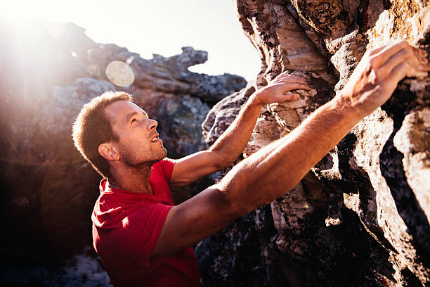 Determination in rock climbing man's face during ascent of mountain Determination and focus showing in rock climbing man's face. He is holding on grip with strong hands and ready to conquer ascent as extreme challenge. bouldering stock pictures, royalty-free photos & images