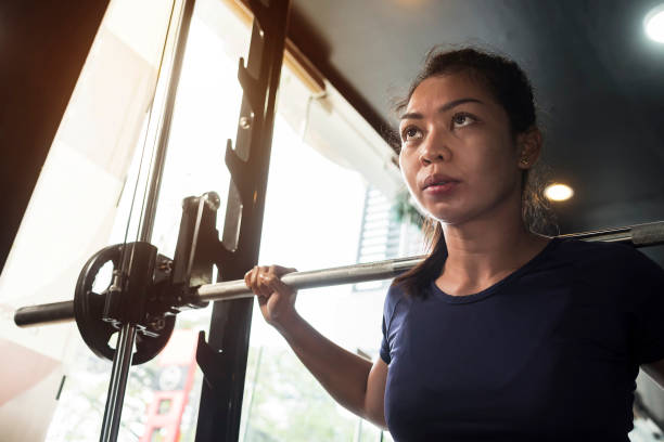 A determined and ready asian lady is ready to do a set of squats. In the middle of a workout session at the gym. stock photo