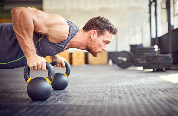 Determined athlete doing push-ups on kettlebells in gym stock photo