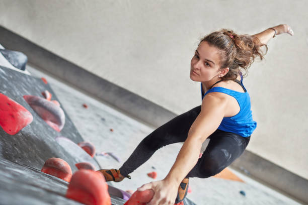 Determined female climbing wall in gym High angle view of determined female climbing wall in gym. Full length of active young woman is exercising. She is in sportswear. bouldering stock pictures, royalty-free photos & images