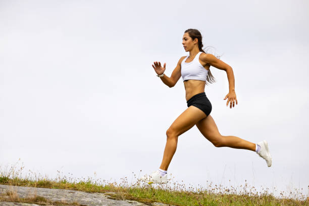 Determined Fit Female Athlete Running On Mountain Against Sky stock photo