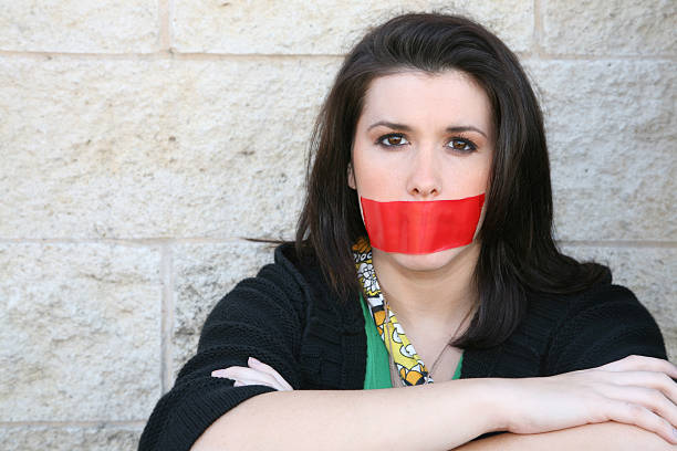 determined young woman sits with red tape over her mouth - plakband mond stockfoto's en -beelden