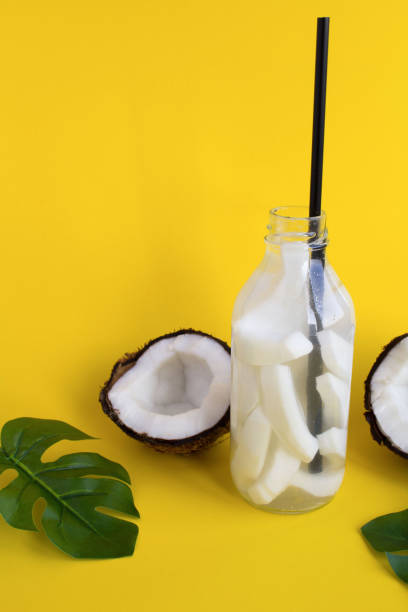 Detox or infused water with coconut in the glass bottle on the yellow  background. Copy space. stock photo