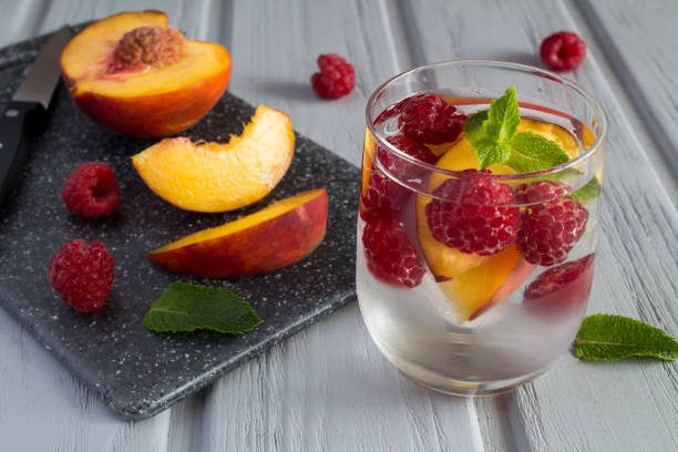 Detox or infused water with raspberry and peach in the drinking glass on the gray wooden background. Close-up. stock photo