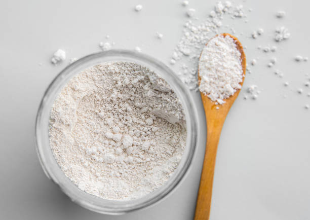 Diatomaceous earth also known as diatomite mixed in glass jar and wood spoon on gray background, studio shot. stock photo