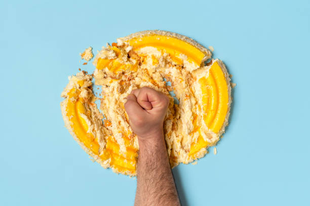 Diet concept with a man fist smashing a cake, top view. Above view with a man's fist smashing a cake. Concept for dieting with an orange whipped cream cake destroyed by a man, top view. smashed cake stock pictures, royalty-free photos & images