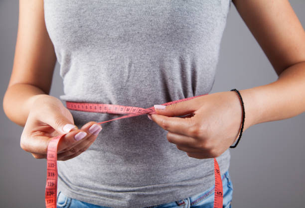Mujer de dieta midiendo cinta sobre fondo gris. Concepto de pérdida de peso. - foto de stock