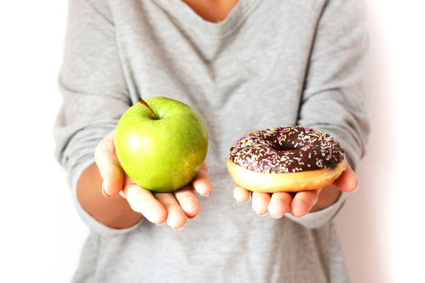 Dieting concept with woman choosing between healthy fruits and donut stock photo