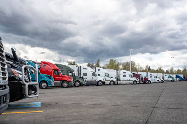 Different big rigs semi trucks with semi trailers standing in long row on truck stop parking lot with stormy sky stock photo