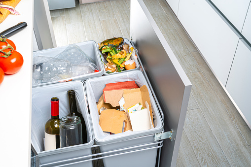 High angle view of an open modern kitchen cabinet with four garbage cans for glass, paper, plastic and organic waste.