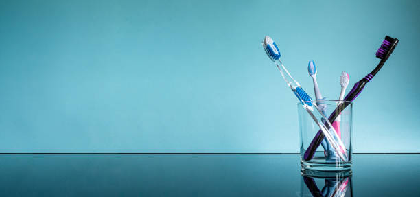 Different large and small toothbrushes for adults and children in a glass in the bathroom on a glass table with a reflection on a blue background. stock photo