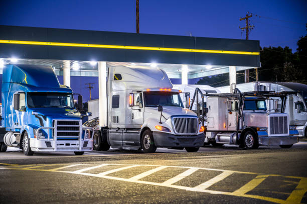 Different make and models big rig semi trucks with semi trailers standing on the truck stop parking lot under the lighted shelter in night stock photo