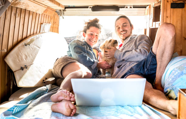 Digital nomad couple with cute dog using laptop on retro mini van...
