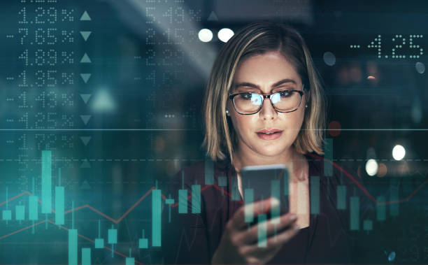 Digitally enhanced shot of an attractive businesswoman using a cellphone superimposed over a graph showing the ups and downs of the stock market stock photo