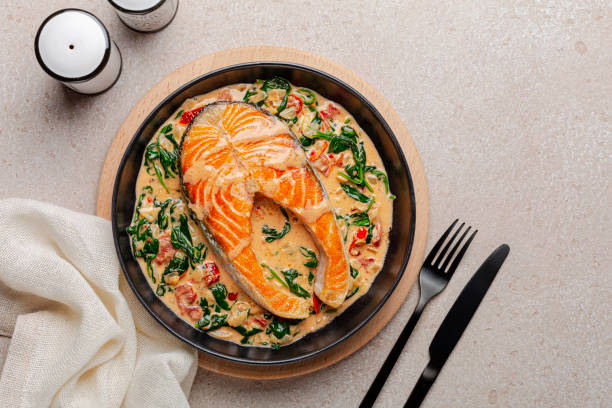 Dinner with creamy garlic butter tuscan salmon. Pan seared salmon in a delicious creamy sauce with spinach and sun dried tomatoes. Top view. Copy space. stock photo