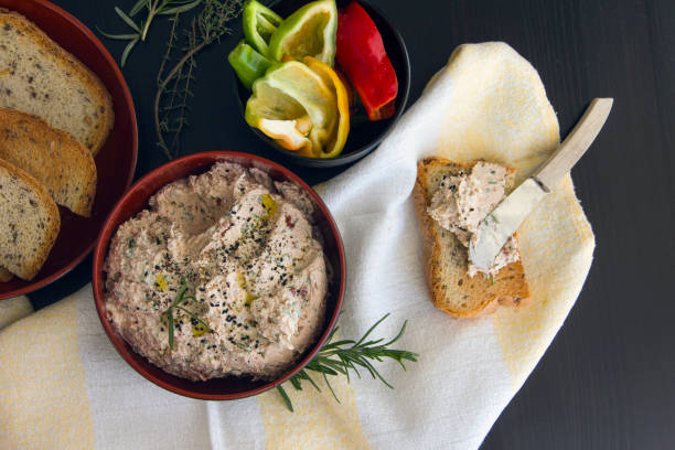 Dip from cottage cheese with sun dried tomatoes, tuna, parsley greens sprinkled with grains of black cumin, served with toast from grain bread on a black background stock photo