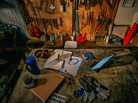 directly above workshop workbench table with documents , digital table, pens, safety equipment and travel mug