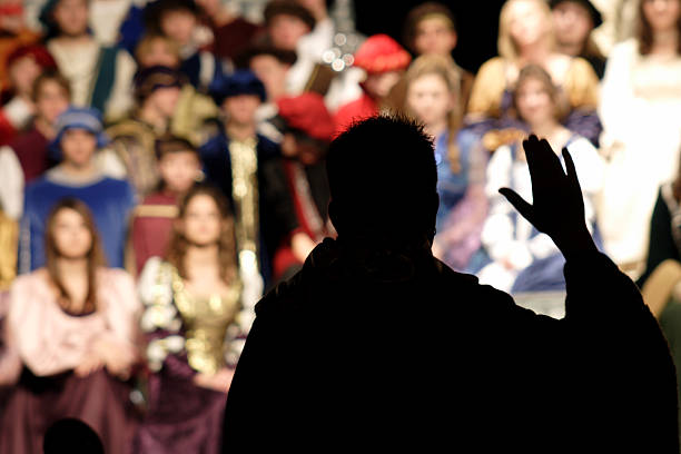 director performance silhouette silhouette of Renaissance musical director in high school with student choir in background acting performance stock pictures, royalty-free photos & images